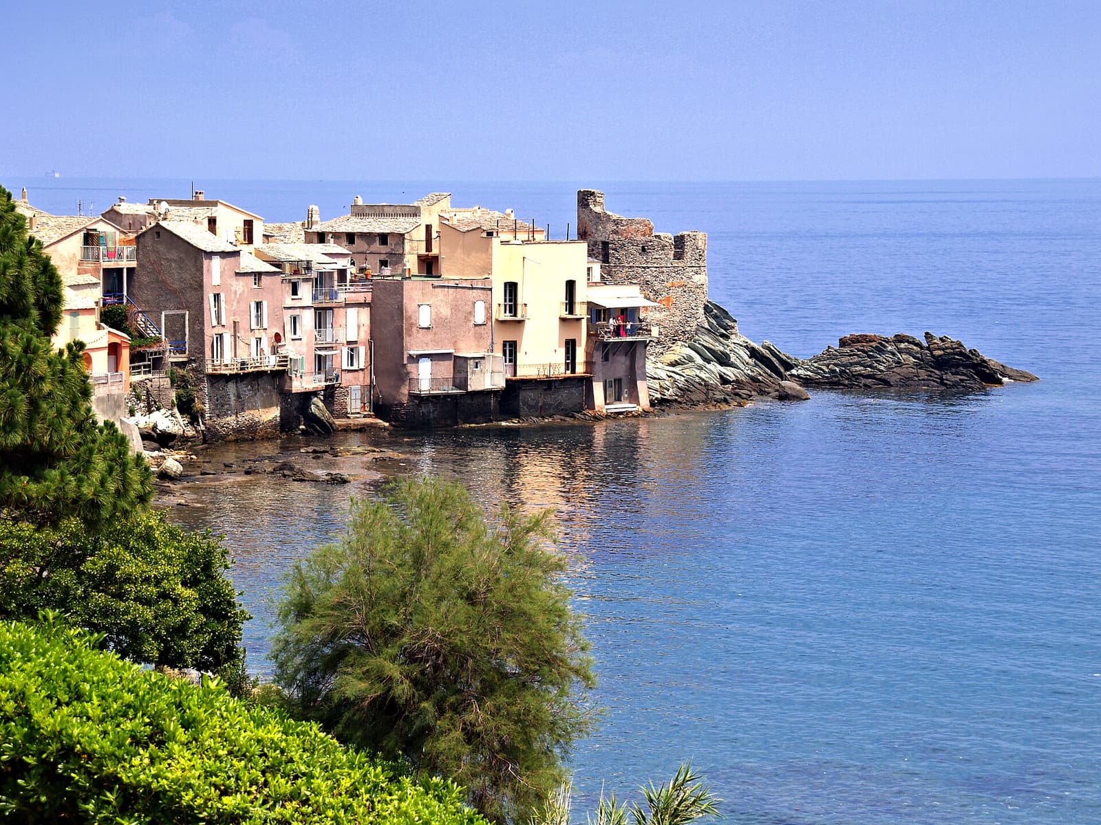 The pastel houses of Erbalunga built on a rocky point, with the ruined Genoese tower at its tip