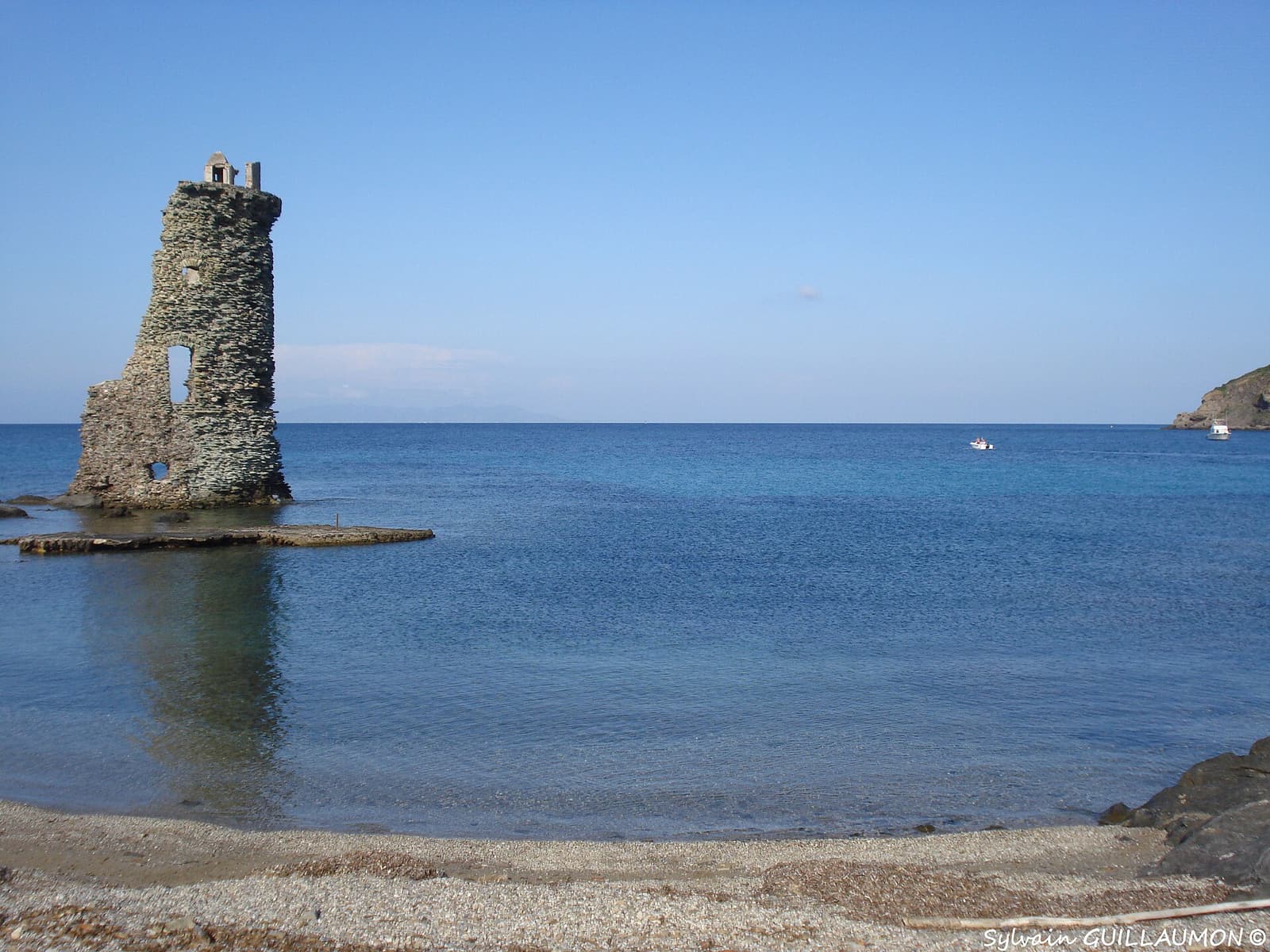 The ruined Genoese tower of Santa Maria standing in shallow water beside a pebble cove on the coast path