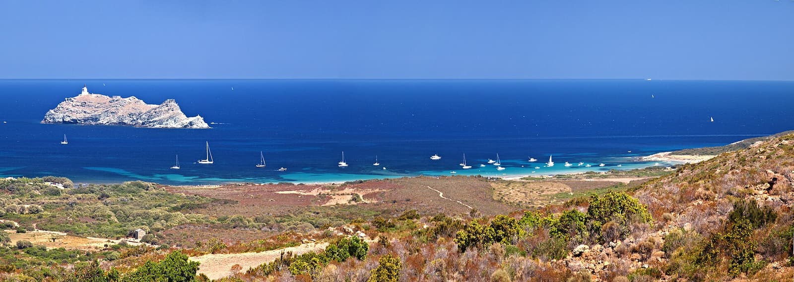 Dunes above the bay of Barcaggio with yachts at anchor and Giraglia island offshore