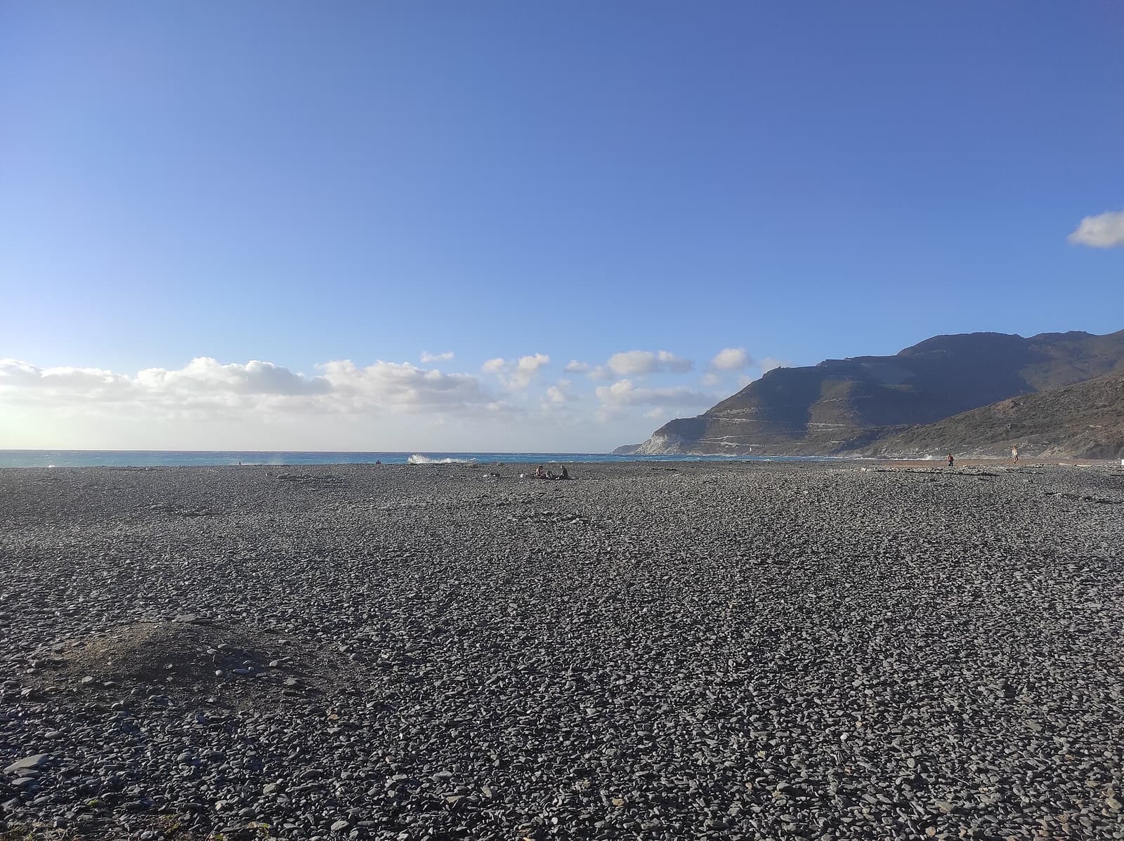 The dark-grey pebbles of Nonza beach stretching away towards the mountains of the west coast